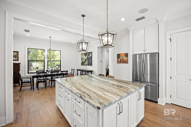 kitchen with light stone counters, visible vents, white cabinetry, freestanding refrigerator, and a center island