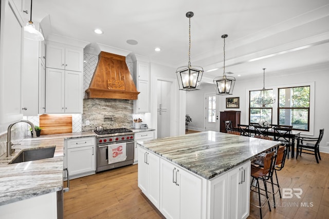 kitchen with custom range hood, hanging light fixtures, premium stove, white cabinetry, and a sink