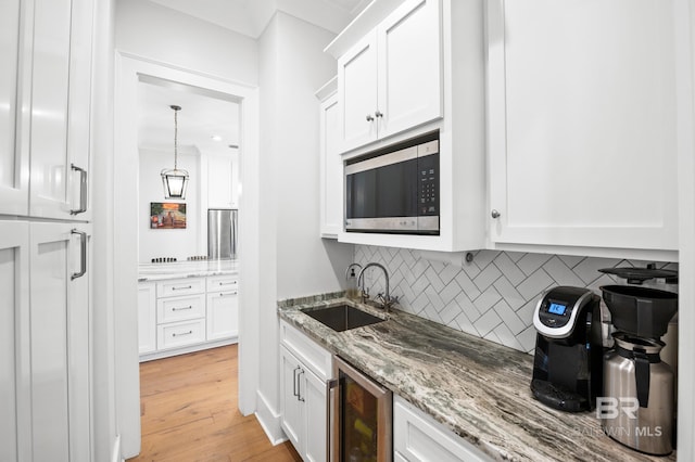 kitchen featuring wine cooler, white cabinets, stainless steel microwave, and a sink