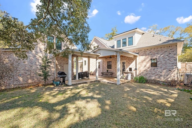 rear view of house with central AC, brick siding, fence, a lawn, and a patio area