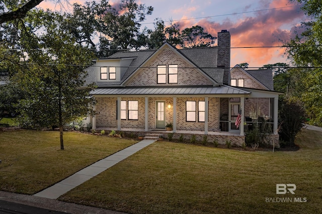 view of front of home featuring a porch, a standing seam roof, brick siding, and a front lawn