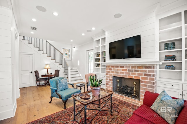 living area with built in shelves, light wood-style flooring, visible vents, stairway, and a brick fireplace