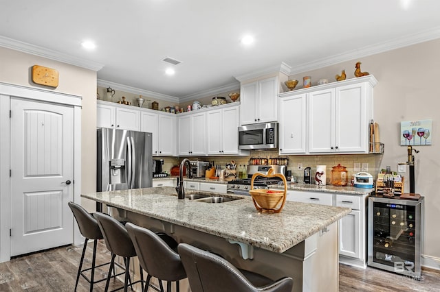 kitchen featuring stainless steel appliances, wine cooler, white cabinetry, and a kitchen island with sink