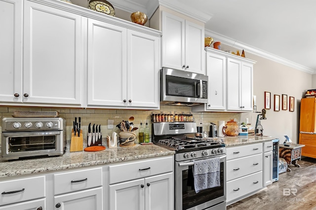 kitchen with stainless steel appliances, white cabinetry, hardwood / wood-style floors, and crown molding