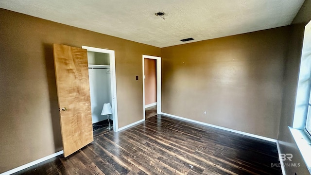 unfurnished bedroom with dark wood-style floors, visible vents, a textured ceiling, and baseboards