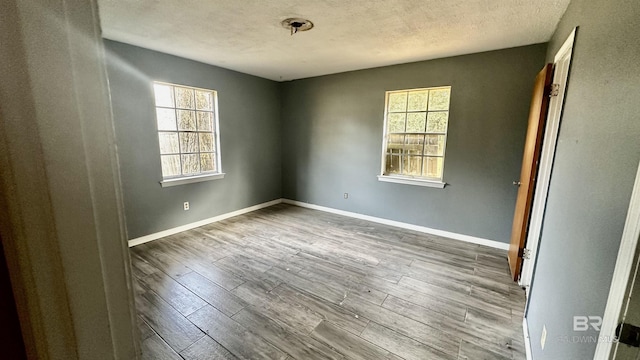 unfurnished room with a textured ceiling, baseboards, and wood finished floors