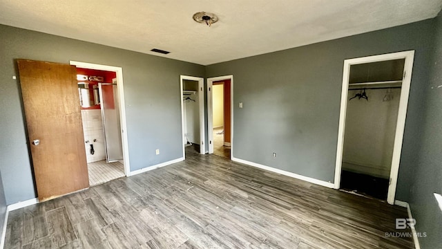 unfurnished bedroom with a walk in closet, a closet, visible vents, and wood finished floors