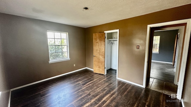 unfurnished bedroom with a textured ceiling, a closet, dark wood finished floors, and baseboards