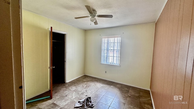 unfurnished bedroom featuring a textured ceiling, baseboards, a ceiling fan, and wooden walls