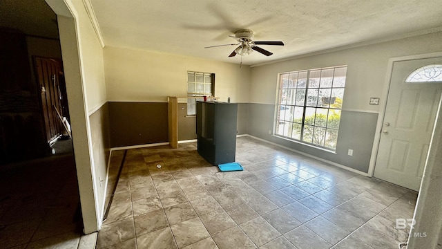 entrance foyer featuring ornamental molding, a textured ceiling, baseboards, and a ceiling fan