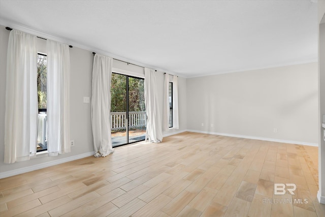 spare room featuring ornamental molding, light wood-type flooring, and baseboards