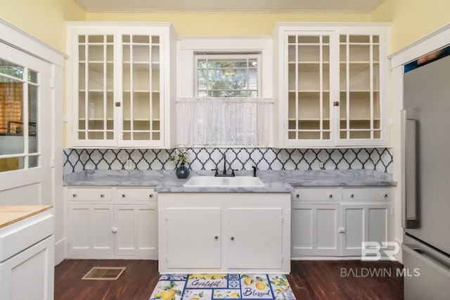 kitchen featuring white cabinets, sink, decorative backsplash, fridge, and light stone counters