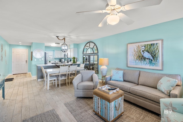 living area with light wood-type flooring, baseboards, and ceiling fan with notable chandelier