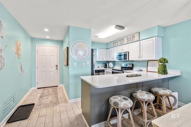 kitchen with a breakfast bar area, a peninsula, stainless steel appliances, light countertops, and white cabinetry