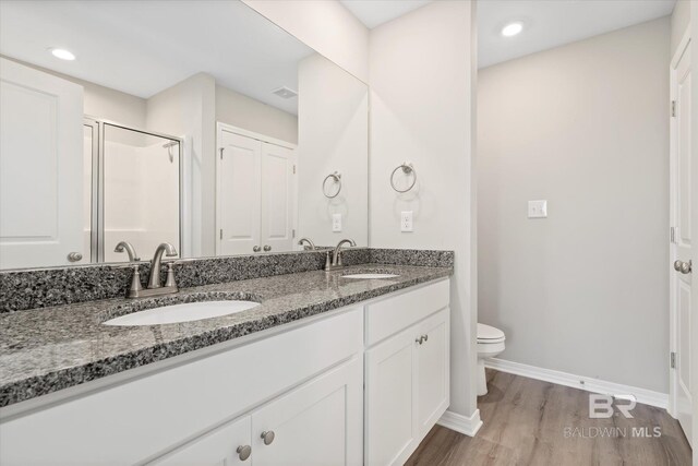 bathroom featuring wood-type flooring, a shower with shower door, vanity, and toilet