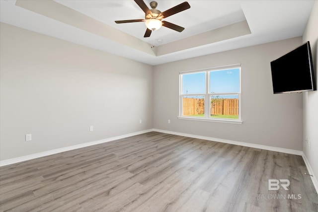 empty room with ceiling fan, light wood-type flooring, and a raised ceiling