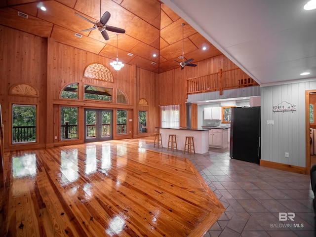 interior space featuring a towering ceiling, ceiling fan with notable chandelier, light wood-type flooring, and black fridge