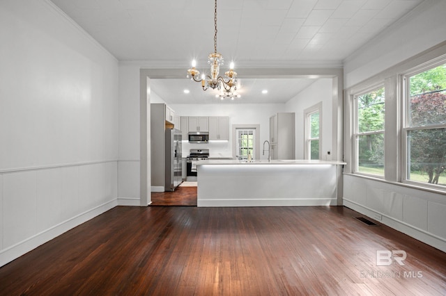 unfurnished living room with visible vents, a sink, dark wood-style floors, a notable chandelier, and ornamental molding