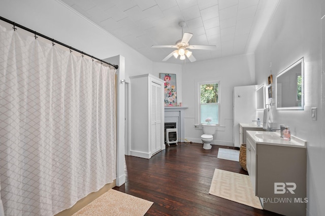 bathroom featuring ceiling fan, a fireplace, vanity, toilet, and hardwood / wood-style floors