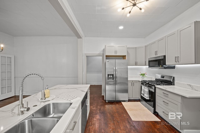kitchen with a sink, dark wood finished floors, appliances with stainless steel finishes, and ornamental molding
