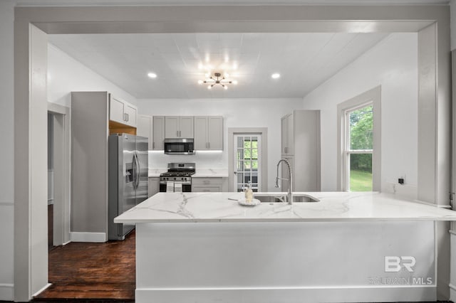 kitchen featuring light stone counters, a sink, stainless steel appliances, a peninsula, and dark wood-style floors