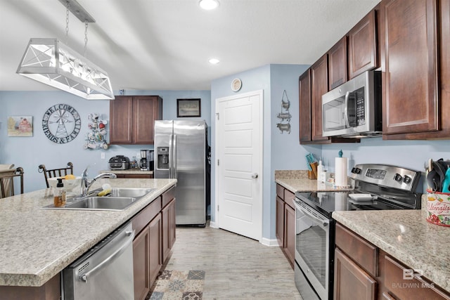 kitchen featuring hanging light fixtures, a center island with sink, light hardwood / wood-style flooring, stainless steel appliances, and sink