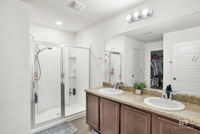 bathroom with dual bowl vanity, an enclosed shower, and wood-type flooring