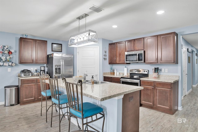 kitchen featuring an island with sink, light hardwood / wood-style flooring, a kitchen bar, and appliances with stainless steel finishes