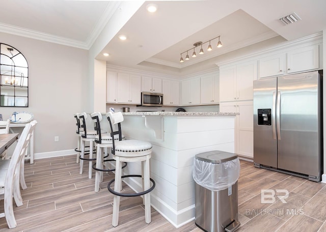 kitchen with light stone counters, track lighting, ornamental molding, white cabinets, and appliances with stainless steel finishes