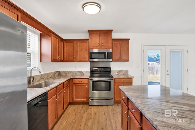 kitchen with light stone countertops, appliances with stainless steel finishes, sink, and light hardwood / wood-style flooring