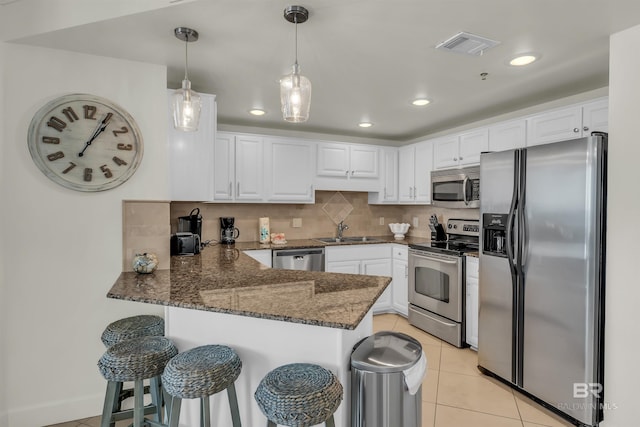 kitchen with a peninsula, a sink, dark stone counters, white cabinetry, and appliances with stainless steel finishes