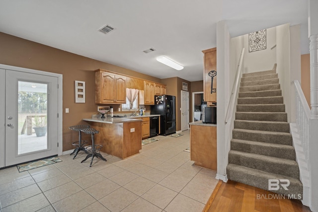 kitchen with sink, kitchen peninsula, a breakfast bar, light tile patterned floors, and black appliances