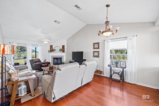 living room with vaulted ceiling, a fireplace, wood-type flooring, and ceiling fan with notable chandelier