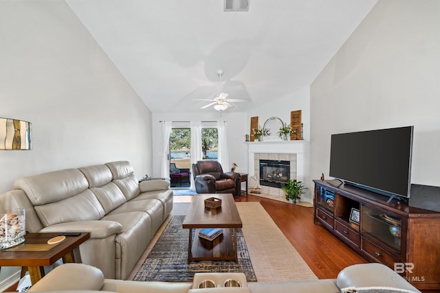 living room with ceiling fan, a tiled fireplace, wood-type flooring, and vaulted ceiling