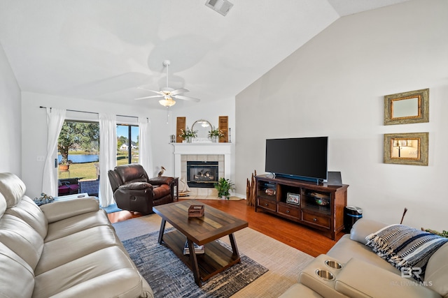 living room with light hardwood / wood-style flooring, vaulted ceiling, ceiling fan, and a tiled fireplace