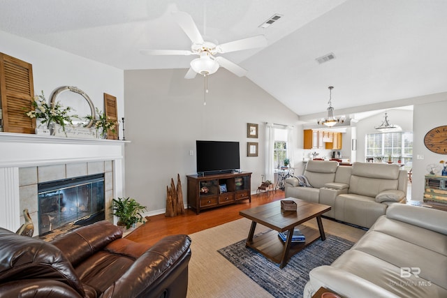 living room featuring ceiling fan with notable chandelier, light wood-type flooring, lofted ceiling, and a tiled fireplace