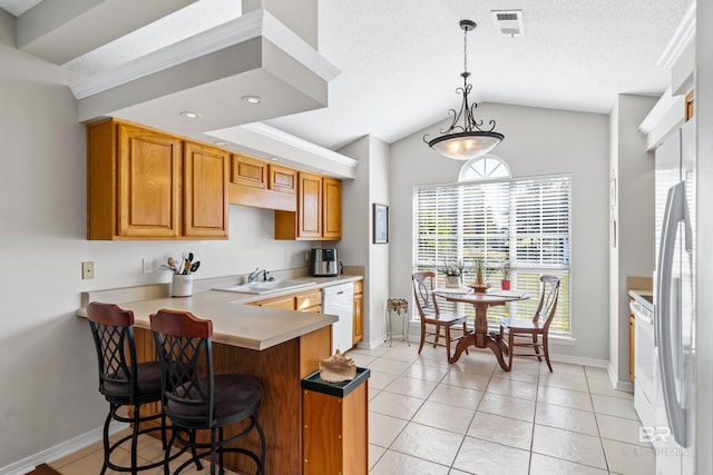 kitchen with kitchen peninsula, white appliances, sink, hanging light fixtures, and a breakfast bar area