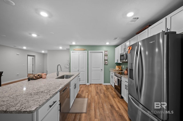 kitchen with white cabinets, visible vents, a center island with sink, stainless steel appliances, and a sink