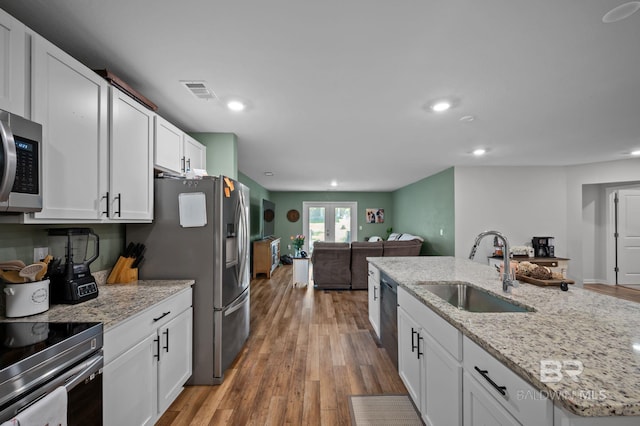 kitchen featuring a sink, open floor plan, light wood-type flooring, appliances with stainless steel finishes, and white cabinetry