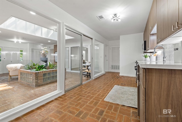 kitchen with brick floor, light countertops, visible vents, brown cabinetry, and a sink