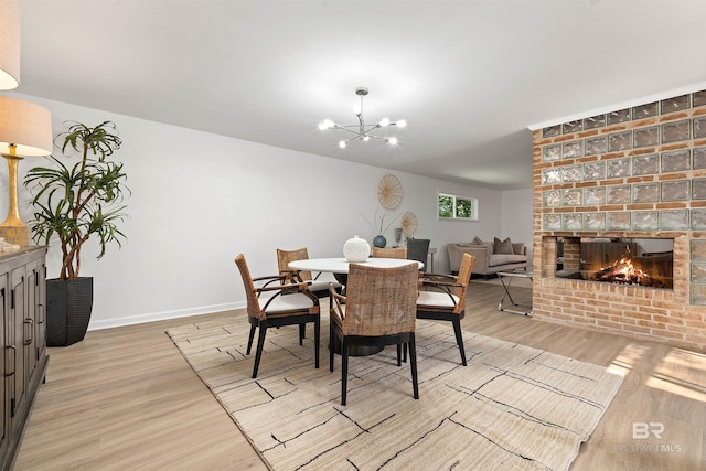 dining space featuring a brick fireplace, an inviting chandelier, and light hardwood / wood-style floors