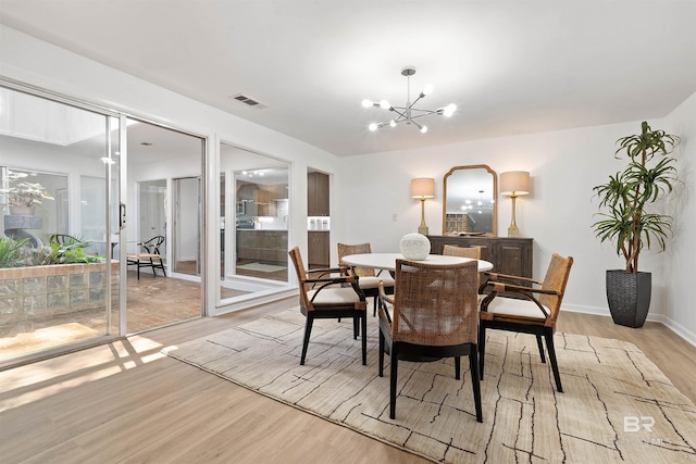 dining room with a notable chandelier, baseboards, visible vents, and light wood-style floors