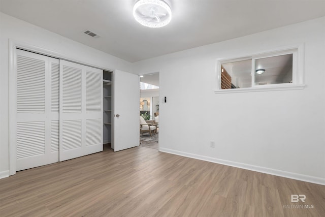 unfurnished bedroom with visible vents, a closet, light wood-style flooring, and baseboards