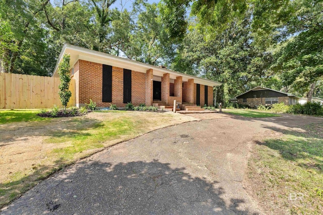 mid-century inspired home with driveway, brick siding, a front lawn, and fence