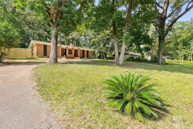 view of front of house with brick siding, a chimney, a front yard, fence, and driveway