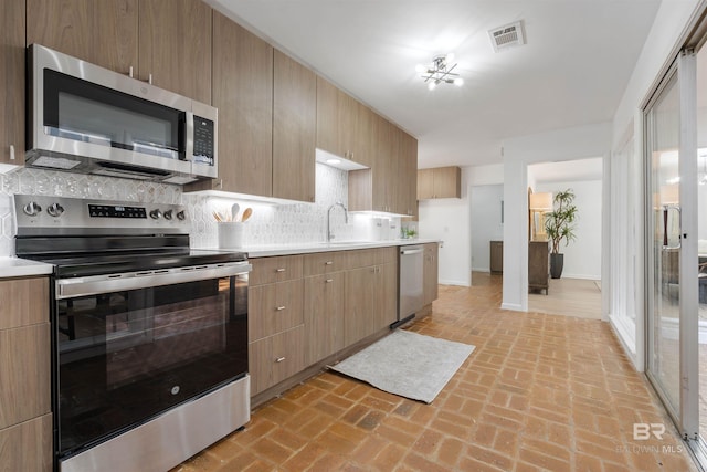 kitchen with modern cabinets, appliances with stainless steel finishes, light countertops, and decorative backsplash