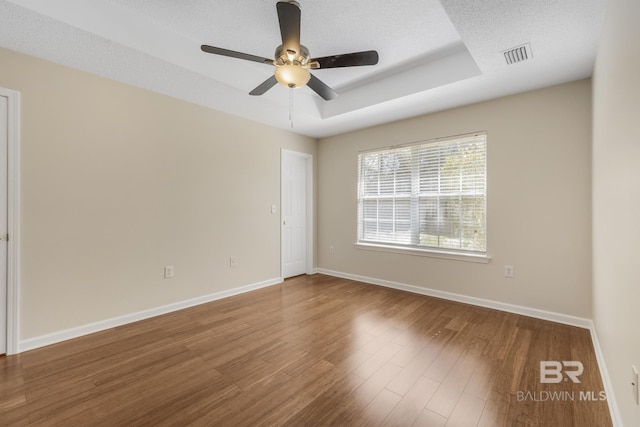 empty room with baseboards, visible vents, wood finished floors, a tray ceiling, and a textured ceiling