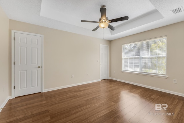 empty room with baseboards, visible vents, a raised ceiling, dark wood-style flooring, and a textured ceiling