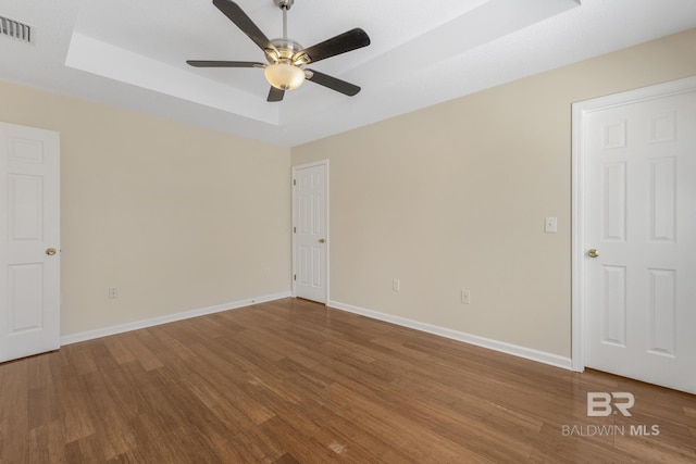 empty room with wood finished floors, a raised ceiling, and visible vents