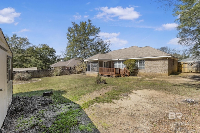 rear view of house with a wooden deck, a sunroom, a fenced backyard, a yard, and brick siding